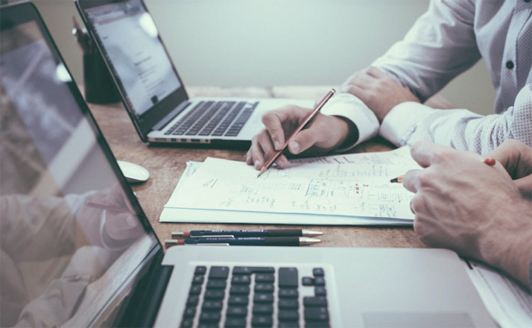 Paper and laptops on a desk being looked at by two people